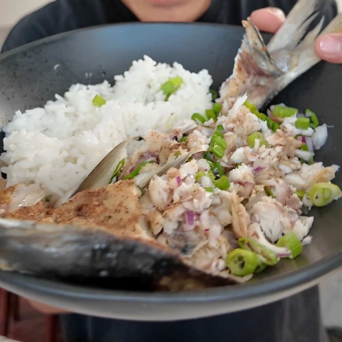 Bangus sisig with white rice in a black bowl, topped with green onions and red onions